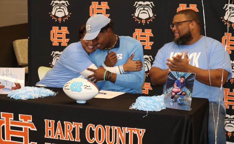 Sunshot by Grayson Williams — Kristi Rucker, left, hugs her son Kaimon Rucker, center, as his father, Kendall Rucker claps during Kaimon’s signing day ceremony on Dec. 18. Kaimon will play college football at the UNiversity of North Carolina.  