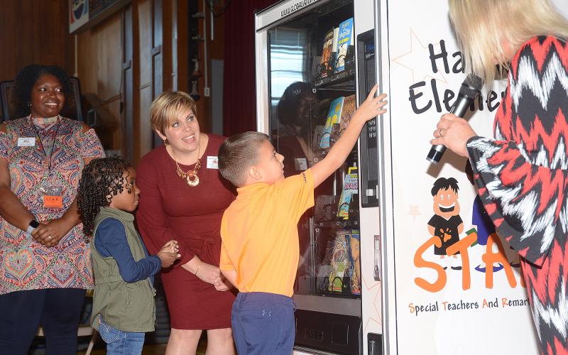 Sunshot by Michael Hall — Kindergartener Duke Swafford reaches up to press the buttons of Inchy’s Bookworm Vending Machine on Oct. 25 at Hartwell Elementary as vice principal Ashley McNeil, from left, second-grader Jordynn Ashmore, media specialist Erin Gaines and principal Lydia Bennett, right, look on.