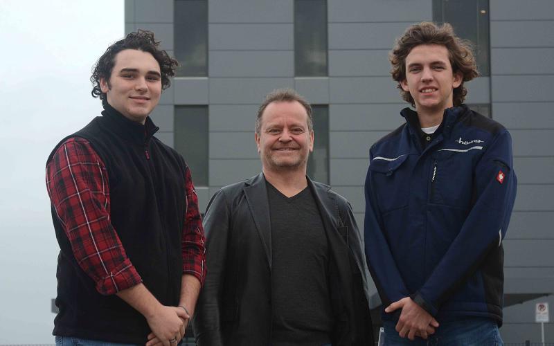 Sunshot by Michael Hall — Hart County High School students Garrett Stone, left, and Lincoln Zemaitis, right, pose for a photo with Dr. Jürgen Häring outside the Häring Precision USA factory currently under construction in the Gateway III industrial park in Hart County.