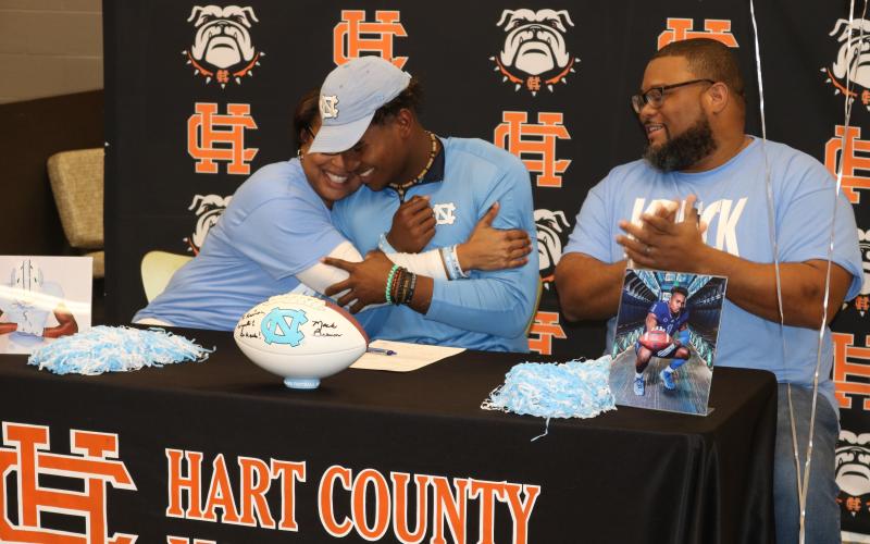 Sunshot by Grayson Williams — Kristi Rucker, left, hugs her son Kaimon Rucker, center, as his father, Kendall Rucker claps during Kaimon’s signing day ceremony on Dec. 18. Kaimon will play college football at the UNiversity of North Carolina.