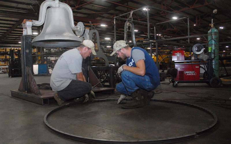 Sunshot from file — Fabritex metal fabricators Martin Neal, left, and Jon Grubbs, right, layout the wheel at Fabritex in 2018 that is now part of a mechanisim used to ring the Victory Bell at Hart County High School. The company refurbished the bell and renewed a longstanding tradition for Hart County Schools, one of many ways Fabritex partners with local schools.