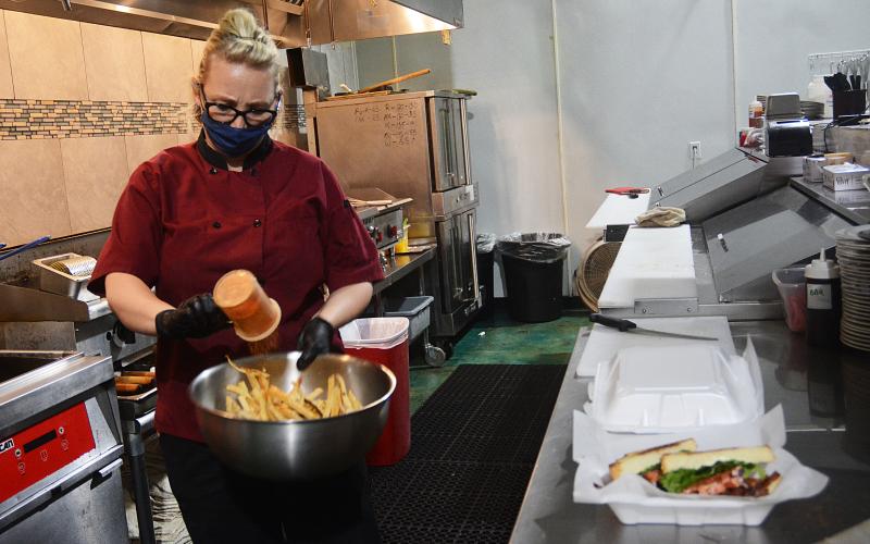 Sunshot by Michael Hall — Hannah Whitsel, owner of Bobbers and Beer Family Steakhouse, seasons French fries for an order on Monday, April 27, at the restaurant. It was the first day she could allow in-person dining in a month.