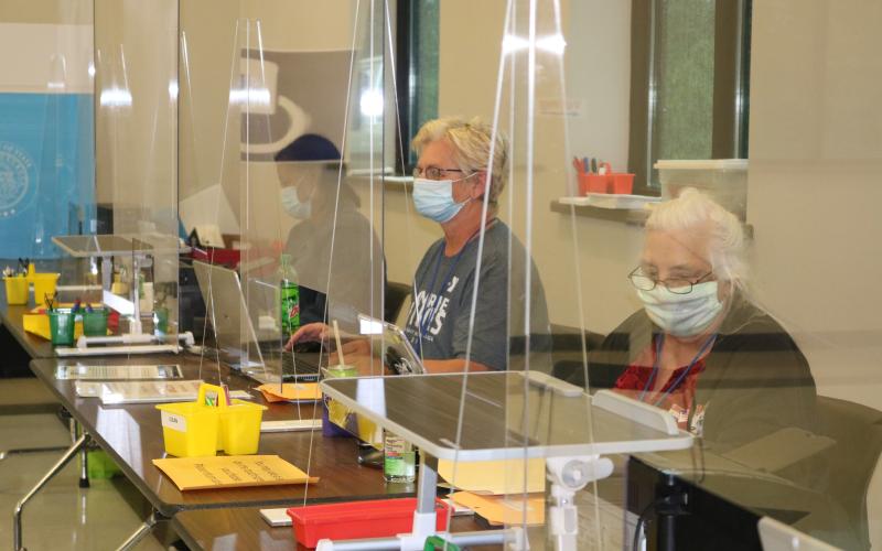 Sunshots by Grayson Williams — Poll workers at the Hart County AgriScience Center sit behind plexiglass windows as they man their stations at the early voting precinct.
