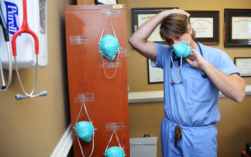Sunshot by Michael Hall Doctor Daniel Gordon, of MedLink, puts on an N-95 mask at the clinic recently. He hangs a mask for each day of the week from his book shelf.