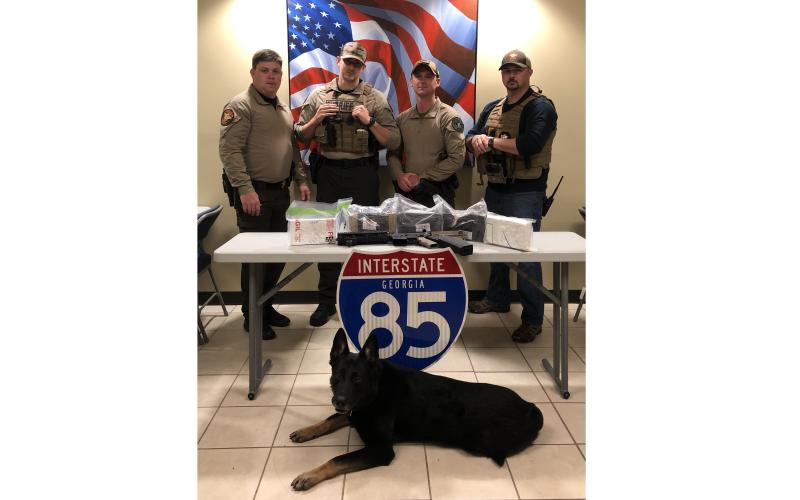Capt. Josh Fowler, deputy Matt Sparrow, deputy Brian Anderson, Inv. Michael Davis and K-9 unit “Chuck” pose for a photo with more than 11 pounds of cocaine and an AR-15 seized from a charter bus traveling on Interstate 85 on Friday.