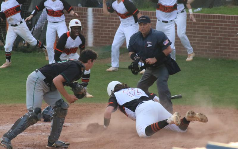 Will Dean slides head-first into home plate and beats the tag to add another run in the Diamond Dogs’ late-inning surge to take a 3-1 victory over region rival Franklin County as fellow Bulldogs celebrate in front of him at home on Tuesday, March 30.