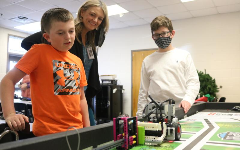 Grayson Williams/The Hartwell Sun South Hart Mindtwister team members Easton Kelley, left, and River Powell, right, eye their robot named “Robie” as it performs a task  and coach Tonya Bridges, center, watches on Thursday, April 22 at South Hart Elementary School.
