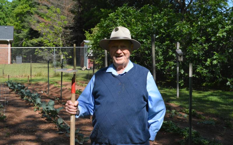 Drew Dotson/The Hartwell Sun - Milner poses with his trusty hoe in front of his backyard garden.
