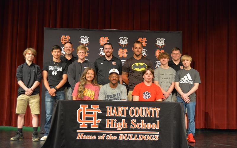 Sunshot by Drew Dotson -Wrestlers Scout Lewis,  left, Elijah Hester, middle,  and Zander Bradsher, right, are seated surrounded by fellow wrestlers and coaches.