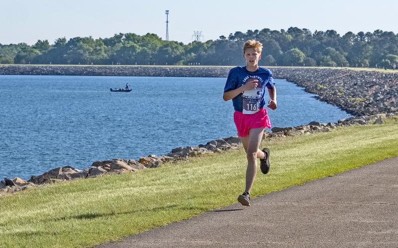 Courtesy of Gwynn Powell - A fisherman goes about his Saturday as normal as Hartwell’s own Zachary Benner, 17, flies past him en route to a first place finish in the 5K with a time of 17:21.