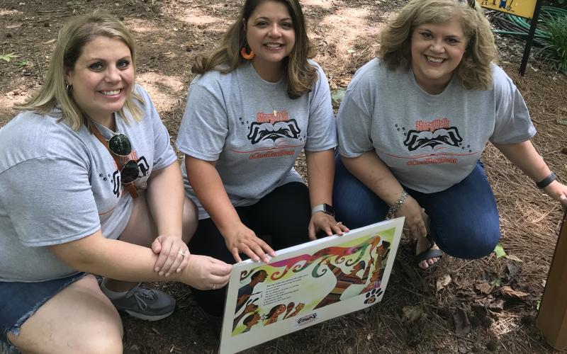 Submitted photo - Hartwell Elementary media specialist Erin Gaines, left, Andina Oglesby, middle, and South Hart media specialist Melissa Camp, right, install a story page along the path at the botanical gardens.