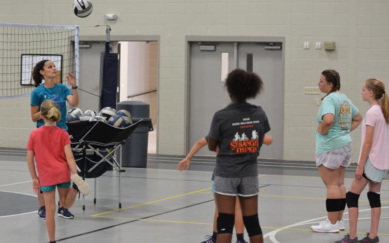 Sports director instructs the campers how to toss the ball before serving at volleyball camp.