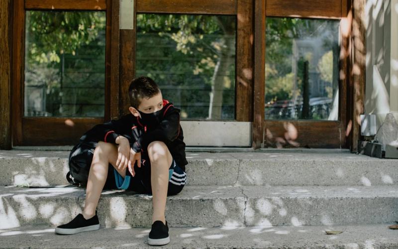 A boy with mask on on the steps waiting for school. Photo credit: Kelly Sikkema