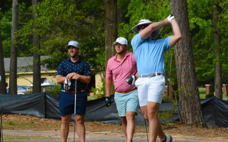 Pictured, John Daniel Gibbs tees off while his partner, Winston Gibbs (left), and Dillon Bowers (middle) watch the ball.