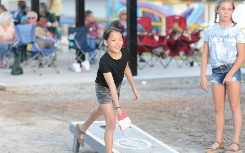Lily Hope Osborne throws a bag in a game of cornhole with Zoey Hill watching.