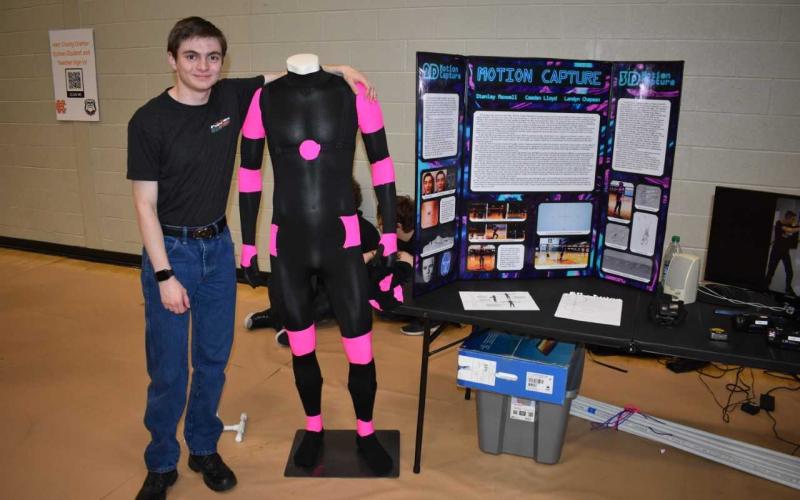 HCHS senior Stanley Maxwell stands alongside the suit that has helped his group for the past four years create 3-D animation.