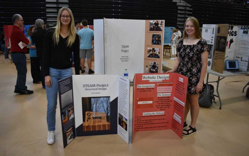 HCHS juniors Ava Carnes (left) and Cassidy Gaines (right) stand alongside their projects. Carnes constructed a bridge out of balsa wood and Gaines created and designed a website.