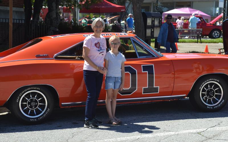 Dan Hunt/The Hartwell Sun - Sue Ackerman and her niece Emmeline Stith pose outside of the Post Office with a 1969 Dodge Charger made up to look like the famed General Lee from the Dukes of Hazzard.