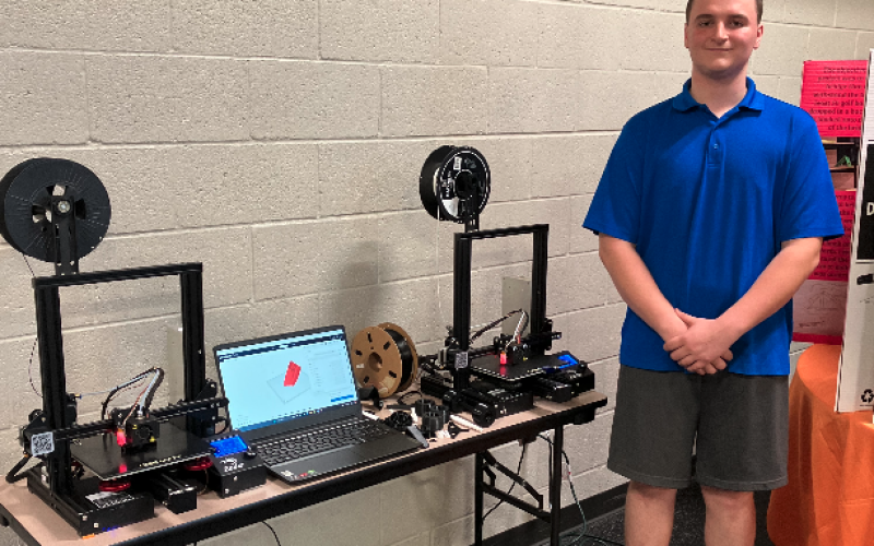 Andrew Pattillo stands proud with his two 3-D printers that were responsible for creating his very own 3-D printed RC car.