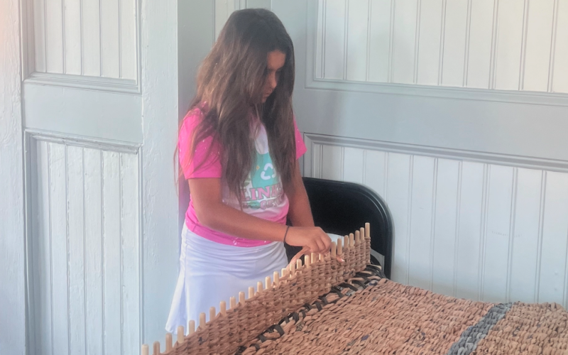 Lila demonstrates how the loom weaves these mats together.