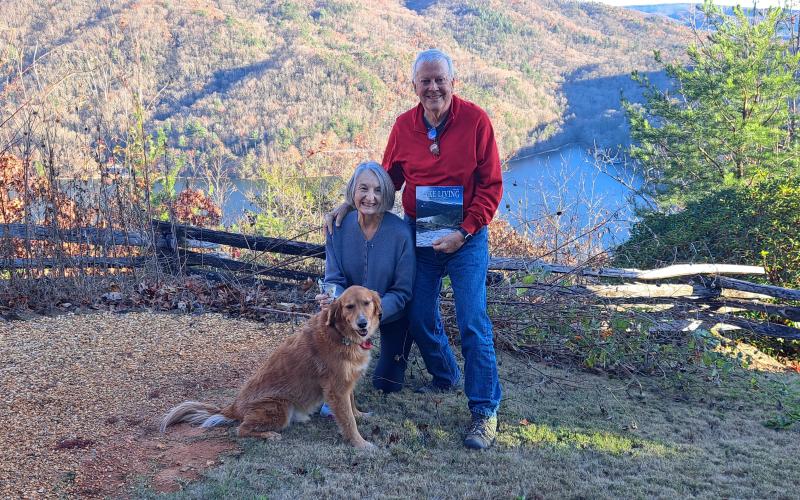 A picture viewing a snowy mountain range and snow-covered fence at Lake Burton taken by Chip Goen of Clayton is now featured on the cover of the Winter 2024 Lake Living magazine. Lin Goen submitted the photograph to the contest. The Goens are pictured here with their dog Charley, the Lake Living magazine cover and $100, with the same backdrop in a different season.