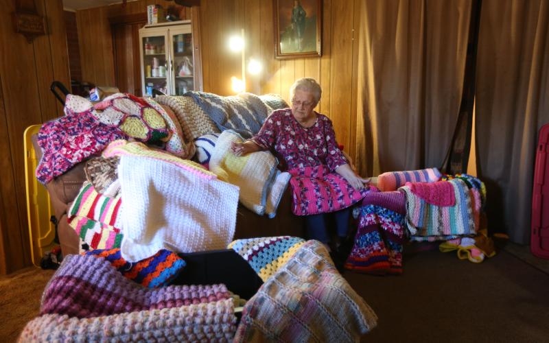 Beverly White sits in her home in the Cross Roads community surrounded by dozens of the brightly colored blankets she’s crocheted over the years after learning the skill from a customer in Jim’s Grill in the early 80s. Right, Beverly sits with her favorite blanket featuring the “Kittens in a Row” pattern.