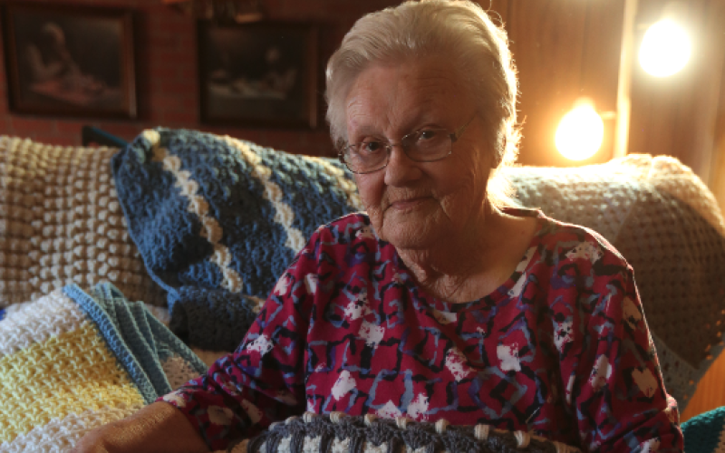 Beverly White sits in her home in the Cross Roads community surrounded by dozens of the brightly colored blankets she’s crocheted over the years after learning the skill from a customer in Jim’s Grill in the early 80s. Right, Beverly sits with her favorite blanket featuring the “Kittens in a Row” pattern.