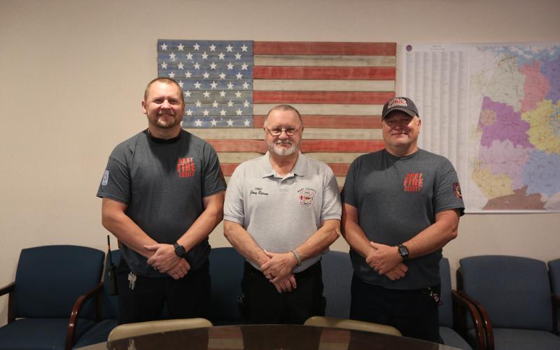 Hart County firefighters (L-R) Matt Evans, a firefighter and paramedic, Chief Jerry Byrum and Teddy Gibson, a firefighter and EMT, stand in front of a flag they made out old firehoses inside the Hart County Fire Department administration office. (Photo/Rose Scoggins)
