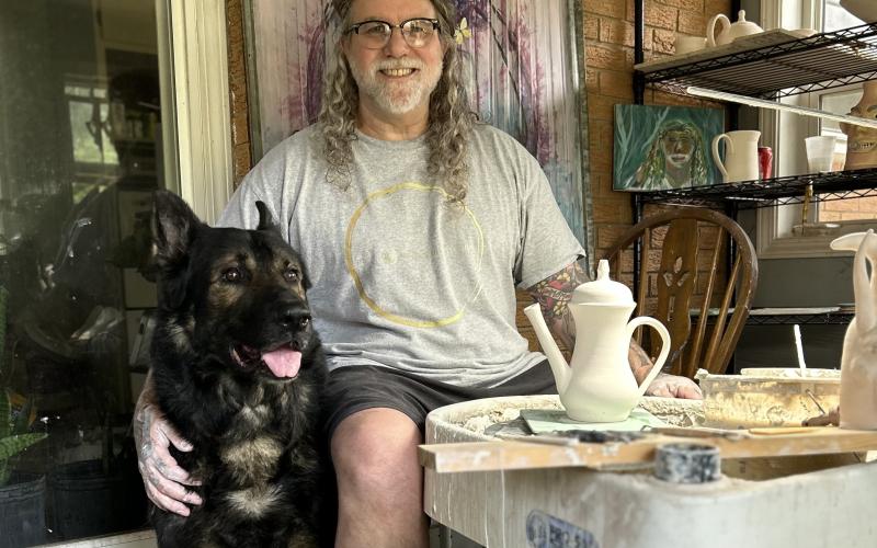 Chad Whitworth, ceramicist and owner of Nevermore Studios, sits at the pottery wheel in his home studio with Judge, a retired k9 german shepherd, by his side. While Whitworth rarely allows anyone else to enter his studio, Judge always keeps Whitworth company during his long hours of throwing on the wheel. (Photo submitted by Whitworth)