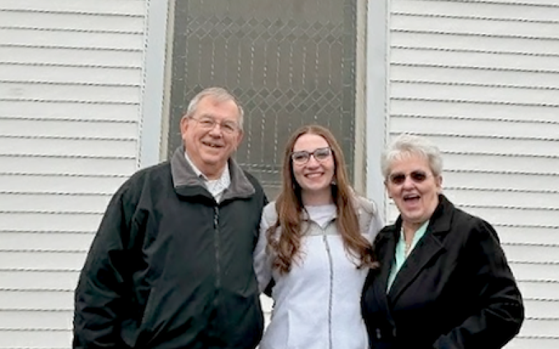 Redwine church members Barry (left) and Theresa Summey (right) pose with their granddaughter, Olivia Summey (center), in front of the new stained glass window Barry completed for the church. Barry credited Olivia for doing the lettering, which features the name of the church, under the cross. Photo submitted by Barry Summey.