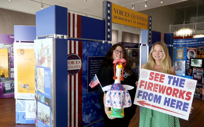 Hart County Chamber of Commerce President and CEO Amanda Brown (left) holding "Nancy Honk," the patriotic porch goose, and Aeva Looney (right), an intern with the Chamber/Hartwell Main Street through the University of Georgia's Archway Program, stand in front of the Smithsonian Exhibit inside the Arts Center of Hartwell Wednesday morning. The pair is advertising a variety of the Pre-4th festivities that will take place alongside the Hartwell Service League's Pre-4th Celebration. Photo by Rose Scoggins.