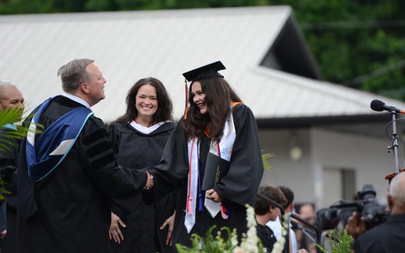 Hart County High School art teacher Amanda Ayers (center) smiles proudly as she watches her daughter, Isabella Ayers (right) receive her diploma from principal Kevin Gaines (left) during Friday's graduation ceremony in Herndon Stadium. Ayers was one of over 240 graduates to receive her diploma during the ceremony. Due to a threat of rain, the event was moved to 6 p.m. from its original time of 8 p.m., and graduates were able to have a rain-free ceremony.  Photo by Benjamin London.