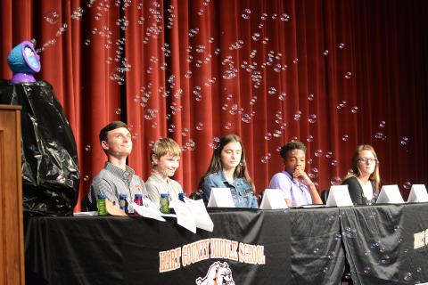 Sunshot by Michael Hall — The 2019 class of REACH Scholars, from left to right, Mason Carey, Ethan Cleveland, Emily Evans, Jashon Gaines and Trinity Wilson, watch bubbles fly as keynote speaker Dink NeSmith, Community Newspapers Inc. president, makes a point about dreams needing to be protected like soap bubbles floating in the wind past jagged rocks.