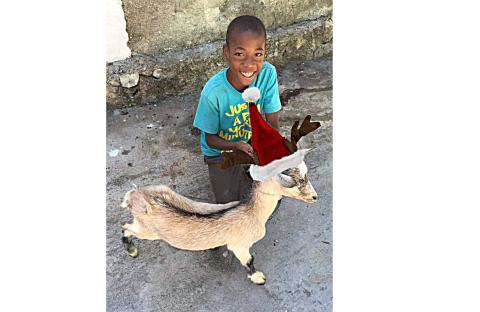 Photo submitted — A Haitian child poses for a photo with his goat that wears a Santa hat. The goat was provided for his family by the Hart County based Acts 1:8 Mission Ministry.