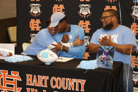 Sunshot by Grayson Williams — Kristi Rucker, left, hugs her son Kaimon Rucker, center, as his father, Kendall Rucker claps during Kaimon’s signing day ceremony on Dec. 18. Kaimon will play college football at the UNiversity of North Carolina.  
