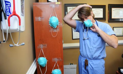 Sunshot by Michael Hall Doctor Daniel Gordon, of MedLink, puts on an N-95 mask at the clinic recently. He hangs a mask for each day of the week from his book shelf.