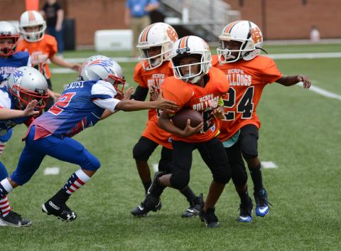Cason Williams, 8U quarterback, runs with the football as Rexdriquez Hill, right, and Christian Marshall, to the left of Williams, look for Patriots to block.