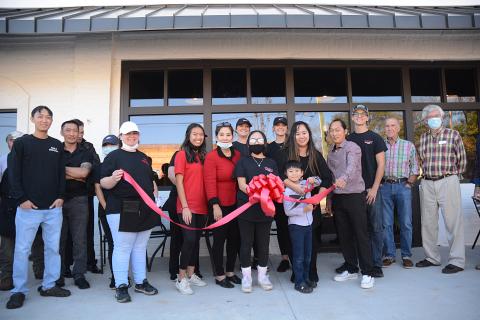 Chance Nguyen holds a pair of giant scissors to cut the ribbon held by his sister Jaslene Nguyen, to the left of Chance, on Monday, Nov. 23, for Little Japan, which is owned by their parents Treena, behind Chance, and Tommy Nguyen. 