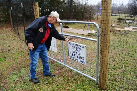 Sunshot by Michael Hall - Frank Spenger adjusts a sign on the gate that was installed as part of a 7-foot-tall deer fence recently constructed around the Hart County Community Garden.