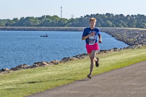 Courtesy of Gwynn Powell - A fisherman goes about his Saturday as normal as Hartwell’s own Zachary Benner, 17, flies past him en route to a first place finish in the 5K with a time of 17:21. 