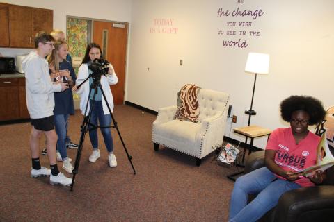 Junior softball player Jakheera Burton, pictured seated right, reads Not Quite Snow White by Ashley Franklin while video production students, pictured left, in the Hart College and Career Academy film a “Books with Bulldogs” episode. 