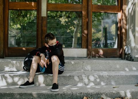 A boy with mask on on the steps waiting for school. Photo credit: Kelly Sikkema