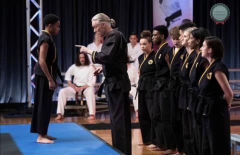 Hartwell Martial Arts instructor Chuck Cawthon, seated second person from left, appears as an extra in several scenes of the hit show “Cobra Kai.” Cawthorn is pictured above in one such scene featuring actor Thomas Ian Griffith (pointing).   