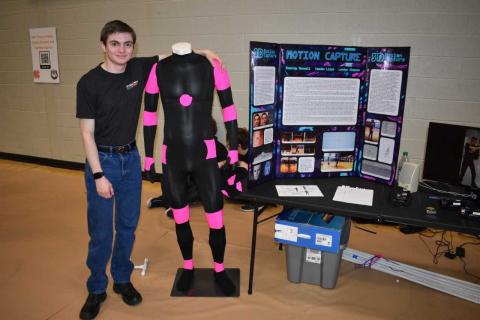 HCHS senior Stanley Maxwell stands alongside the suit that has helped his group for the past four years create 3-D animation.