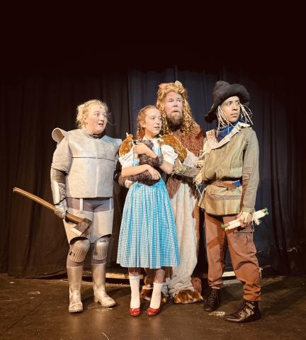 The Ruby Cast during rehearsals for The Wizard of Oz. Pictured from left to right is Morgan Haymes as the Tin Man, Lainey Dickson as Dorothy, Seth Howard as the Cowardly Lion, and August Thompson as the Scarecrow.