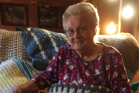 Beverly White sits in her home in the Cross Roads community surrounded by dozens of the brightly colored blankets she’s crocheted over the years after learning the skill from a customer in Jim’s Grill in the early 80s. Right, Beverly sits with her favorite blanket featuring the “Kittens in a Row” pattern. 