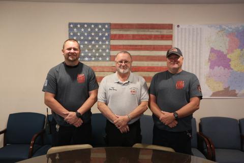 Hart County firefighters (L-R) Matt Evans, a firefighter and paramedic, Chief Jerry Byrum and Teddy Gibson, a firefighter and EMT, stand in front of a flag they made out old firehoses inside the Hart County Fire Department administration office. (Photo/Rose Scoggins)