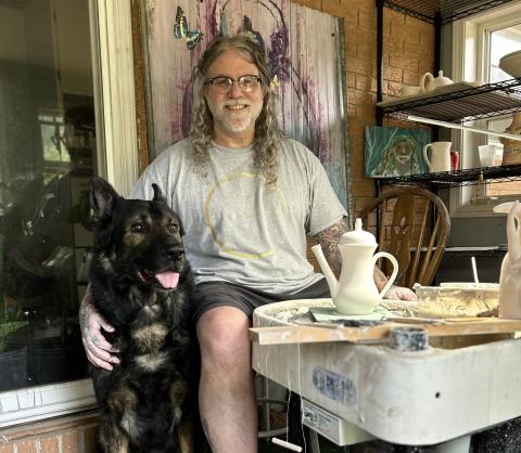 Chad Whitworth, ceramicist and owner of Nevermore Studios, sits at the pottery wheel in his home studio with Judge, a retired k9 german shepherd, by his side. While Whitworth rarely allows anyone else to enter his studio, Judge always keeps Whitworth company during his long hours of throwing on the wheel. (Photo submitted by Whitworth)