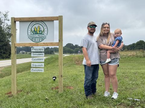 The Saxon family (L-R) Garrett Saxon, Breanna Saxon and Annalee Saxon stand next to the Saxon’s Produce sign located at 8701 Bowman Highway in Dewy Rose. Saxon’s Produce first opened on Memorial Day 2025 and sells double-yolk eggs, pickles and produce. (Photo/Adriana Cascio)