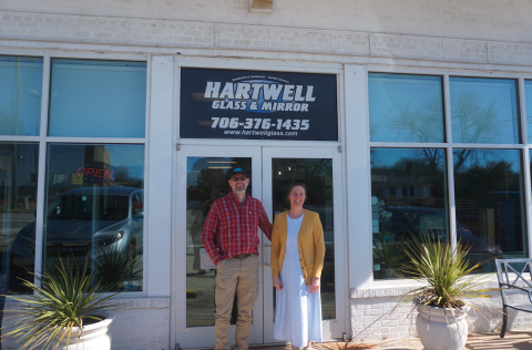 Lyle (left) and Margaret (right) Koehn standing in front of their business, Hartwell Glass and Mirror. The shop is turning 30 this year. Photo by Madison Linton.